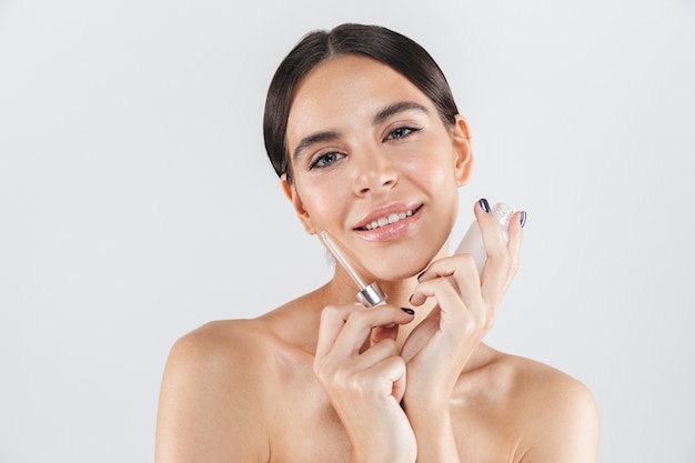 Beauty portrait of an attractive healthy woman standing isolated over white wall, applying body oil