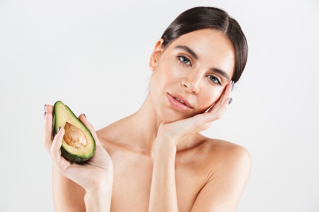 Beauty portrait of an attractive healthy woman standing isolated over white wall, posing with avocado