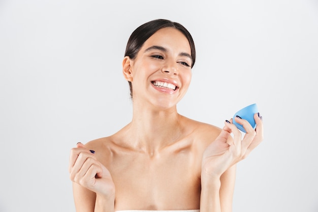 Beauty portrait of an attractive healthy woman standing isolated over white wall, showing makeup sponge