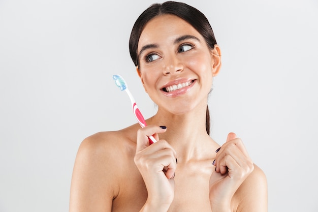 Beauty portrait of an attractive healthy woman standing isolated over white wall, showing a toothbrush