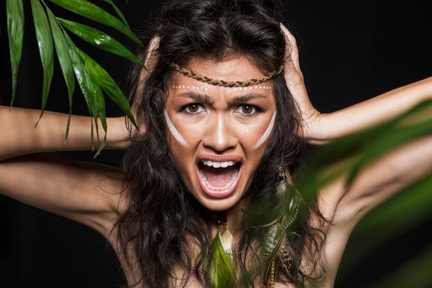 Beauty portrait of an attractive young brunette woman wearing tribal accessories posing with tropical leaves isolated, screaming