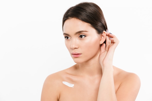 Beauty portrait of beautiful asian woman looking aside with cream on her body, isolated over white