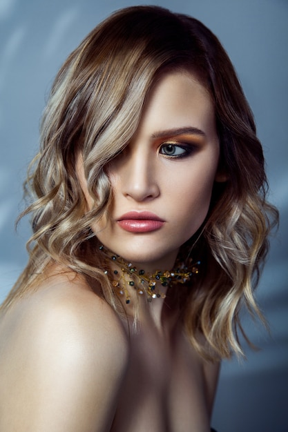 Photo beauty portrait of beautiful fashion model with makeup, colored wavy hairstyle and accessories on her neck. studio shot on blue background. .