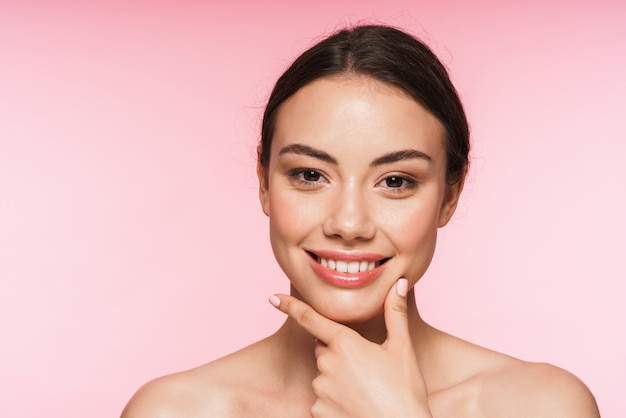 Beauty portrait of a beautiful smiling young topless brunette woman standing isolated on pink, posing