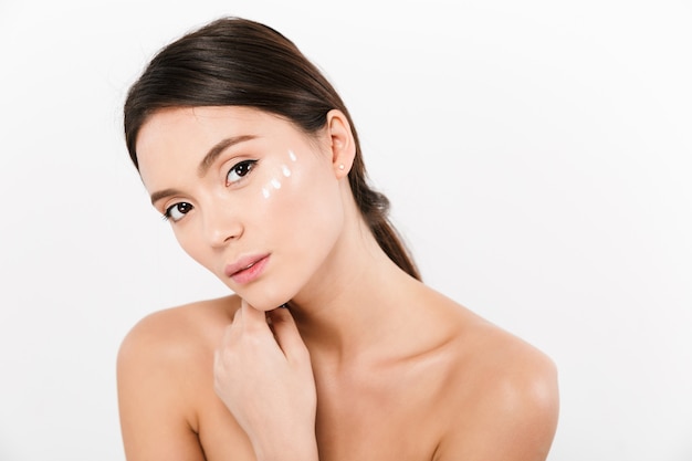 Beauty portrait of gentle asian woman with cream on her face, isolated over white