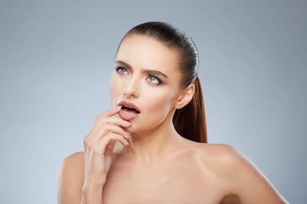 Beauty portrait of girl looking aside thinking about something. Head and shoulders of contemplated woman touching her lower lip. Natural make up, studio, true emotions