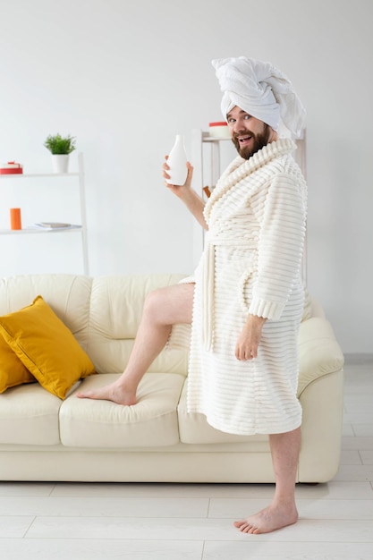 Beauty portrait of handsome beautiful guy in towel and bathrobe holding tube of body cream lotion in hand. Spa, body and skin care for man concept.