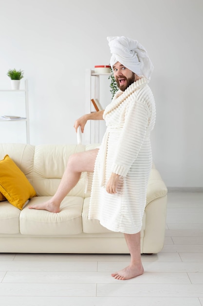 Beauty portrait of handsome beautiful guy in towel and bathrobe holding tube of body cream lotion in hand. Spa, body and skin care for man concept.