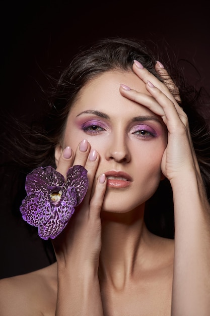 Beauty portrait of a nude woman with a purple flower in her hands on a dark background. Natural cosmetics, natural makeup