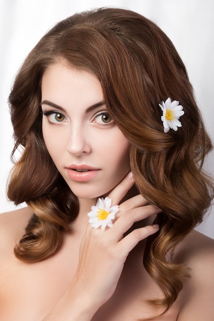 彼女の顔に触れるカモミールの花を持つ若い女性の美しさの肖像画