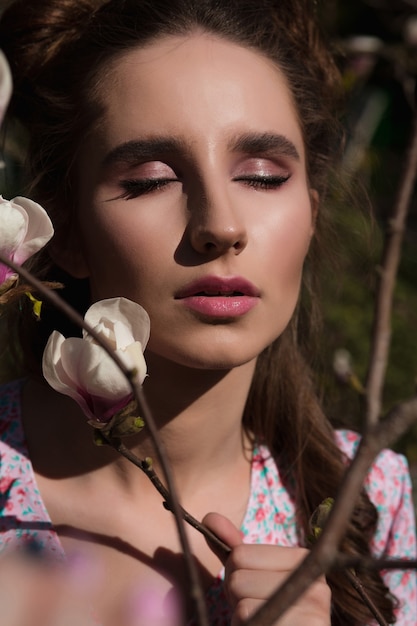 Foto ritratto di bellezza di una bella donna castana in posa vicino all'albero di magnolia in fiore in abito alla moda