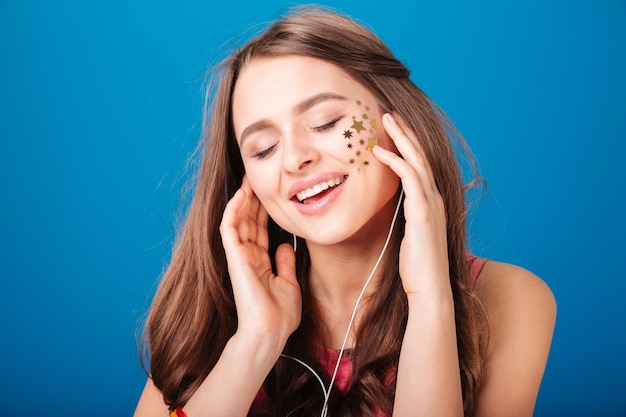Beauty portrait of pretty happy young woman with star shaped decoration on cheek over blue background