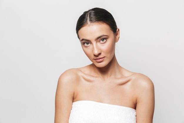 Beauty portrait of a pretty young woman wrapped in towel standing isolated, posing