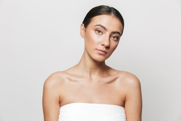 Beauty portrait of a pretty young woman wrapped in towel standing isolated, posing