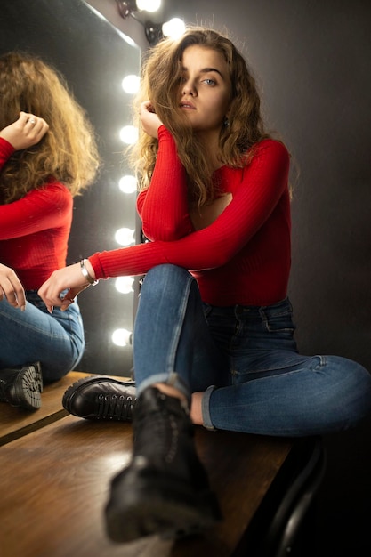 Beauty portrait of a sensual young woman with curly hair sitting on wooden table posing near mirror