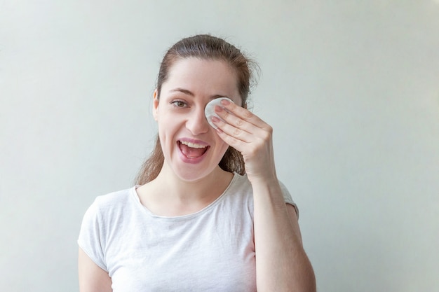 Beauty portrait of smiling woman with soft healthy skin removing make up with cotton pad isolated on white background.