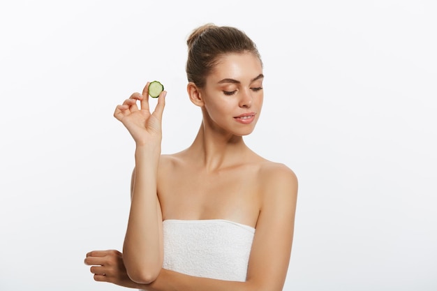 Beauty portrait of smiling woman with towel on head and slice of cucumber in hand isolated on white