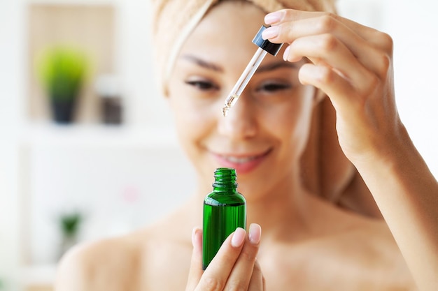 Beauty portrait of smiling young woman girl holding pipette with cosmetic oil or serum near face