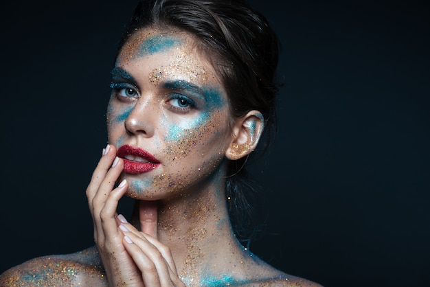 Beauty portrait of tender young woman with shimmering makeup touching her lips over black surface