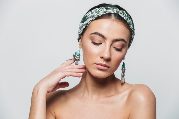 Beauty portrait of a topless young beautiful woman wearing headband and earrings standing isolated