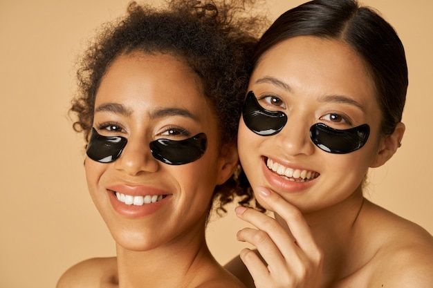Портрет красоты двух возбужденных молодых женщин, позирующих с нанесенными черными пятнами под глазами