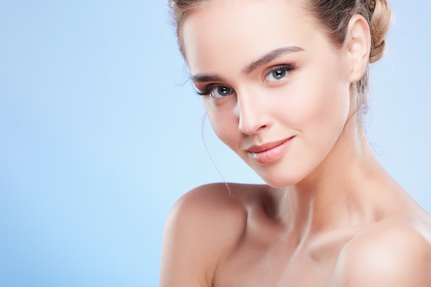 Beauty portrait of woman looking at camera with light smile, closeup. Head and shoulders of woman with nude make-up, turned aside, beauty concept