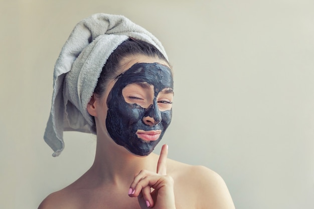 Beauty portrait of woman in towel on head applying black nourishing mask on face, white background isolated. Skincare cleansing eco organic cosmetic spa relax concept