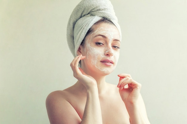 Ritratto di bellezza della donna in asciugamano sulla testa con maschera nutriente bianca o crema sul viso, sfondo bianco isolato. cura della pelle pulizia eco cosmetici biologici spa relax concept