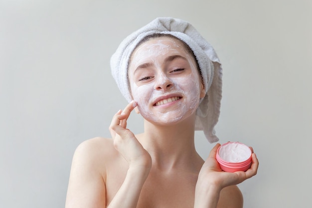 Ritratto di bellezza di donna in asciugamano sulla testa con maschera nutriente bianca o crema su sfondo bianco viso isolato