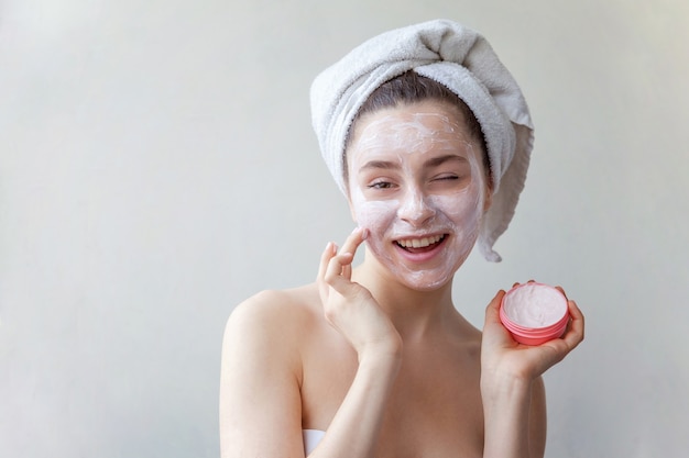 Ritratto di bellezza della donna in asciugamano sulla testa con maschera nutriente bianca o crema sul viso