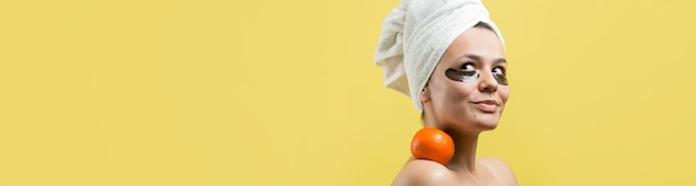 Beauty portrait of woman in white towel on head with gold nourishing mask on face Skincare cleansing eco organic cosmetic spa relax concept A girl stands with her back holding an orange mandarin