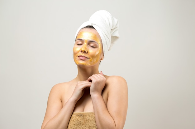 Портрет красоты женщины в белом полотенце на голове с золотой питательной маской на лице Уход за кожей