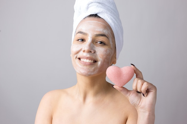 Beauty portrait of woman in white towel on head  with a sponge for a body in view of a pink heart