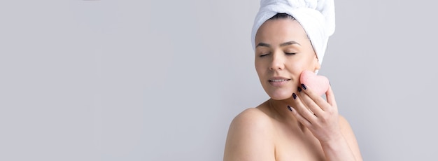 Beauty portrait of woman in white towel on head with a sponge for a body in view of a pink heart