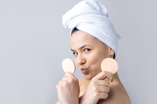 Beauty portrait of woman in white towel on head with a sponge for a body in view of a pink heart