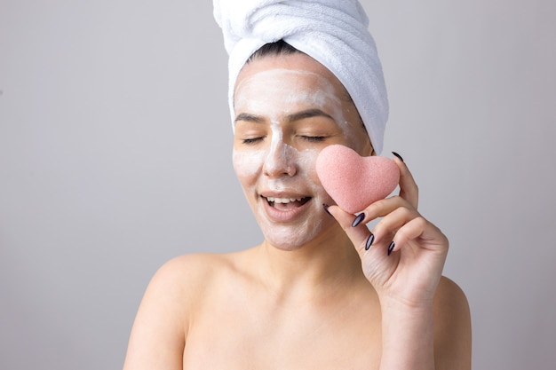 Beauty portrait of woman in white towel on head  with a sponge for a body in view of a pink heart