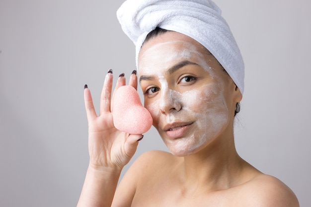 Beauty portrait of woman in white towel on head  with a sponge for a body in view of a pink heart