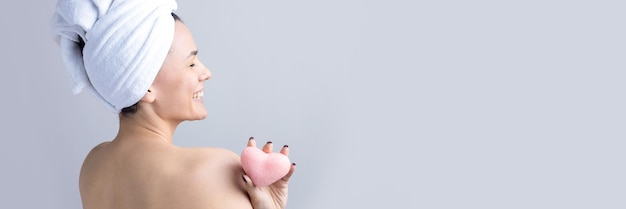 Beauty portrait of woman in white towel on head with a sponge for a body in view of a pink heart