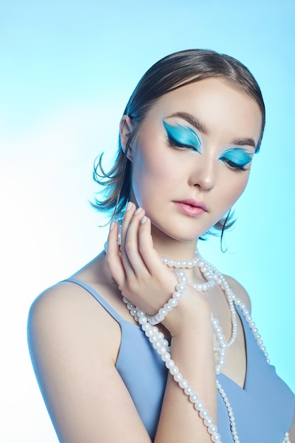 Beauty portrait of a woman with blue eyes a blue dress and a blue background Art makeup Professional makeup and cosmetics for the face Sophisticated art portrait style