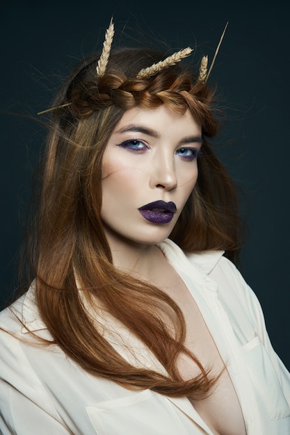 Beauty portrait woman with pigtail on her head and ears of wheat. Bright dark lipstick and eye makeup, smooth facial skin. Hair fluttering in wind, wheat in beautiful hands woman