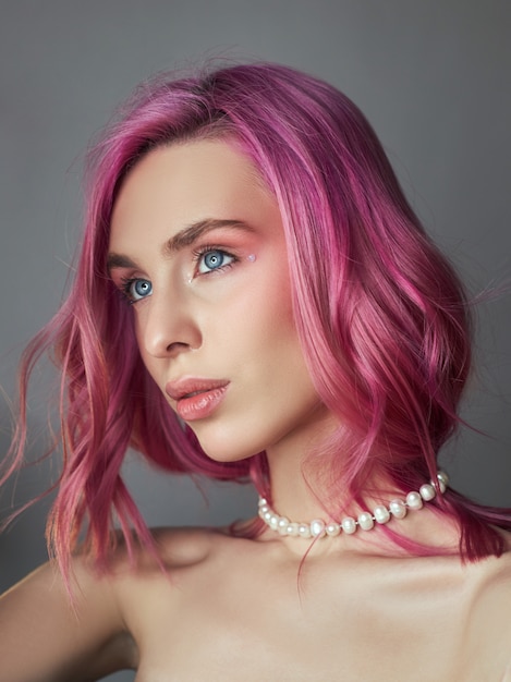 Beauty portrait woman with pink hair, creative vivid coloring. Bright colored highlights and shadows color on the face, a girl with jewelry. Dyed hair in the wind