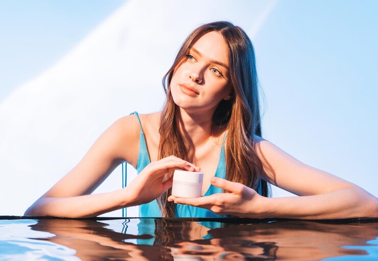 Beauty portrait of young girl fashion model with cosmetic cream in hands on blue background