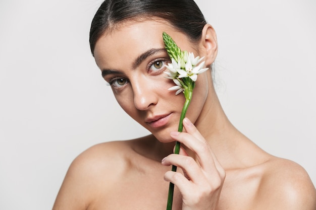 Beauty portrait of a young healthy attractive brunette woman standing isolated holding flower plant near her face