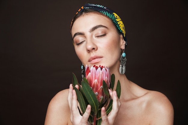 Beauty portrait of a young healthy attractive brunette woman standing isolated holding flower plant near her face