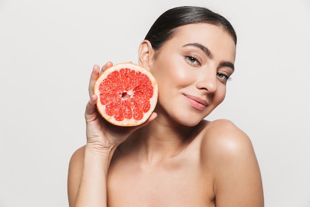 Beauty portrait of a young healthy attractive brunette woman standing isolated, posing with a grapefruit