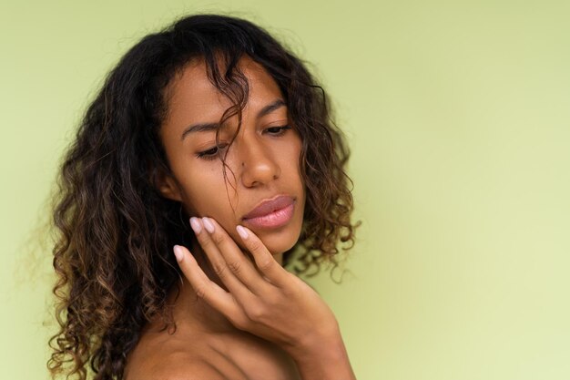 Beauty portrait of young topless african american woman with bare shoulders on green background with perfect skin and natural makeup