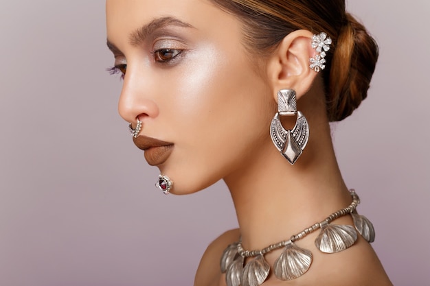 Beauty portrait of young woman with beautiful makeup, looks in profile, earrings and necklace jewelry, arranged hair.