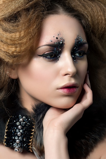 Beauty portrait of young woman with fashion makeup with rhinestones touching her face.. Carnival or party makeup