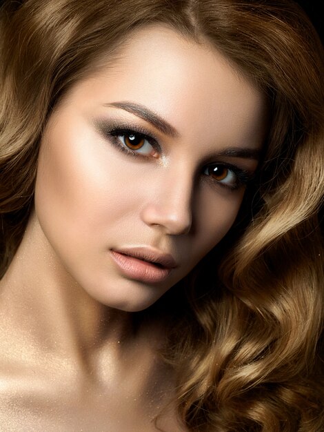 Beauty portrait of young woman with golden makeup. Perfect skin and fashion makeup, smokey eyes. Sensuality, passion, trendy luxurious makeup concept.