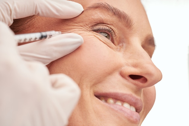 beauty procedure close up of a beautiful mature woman receiving hyaluronic acid injection by